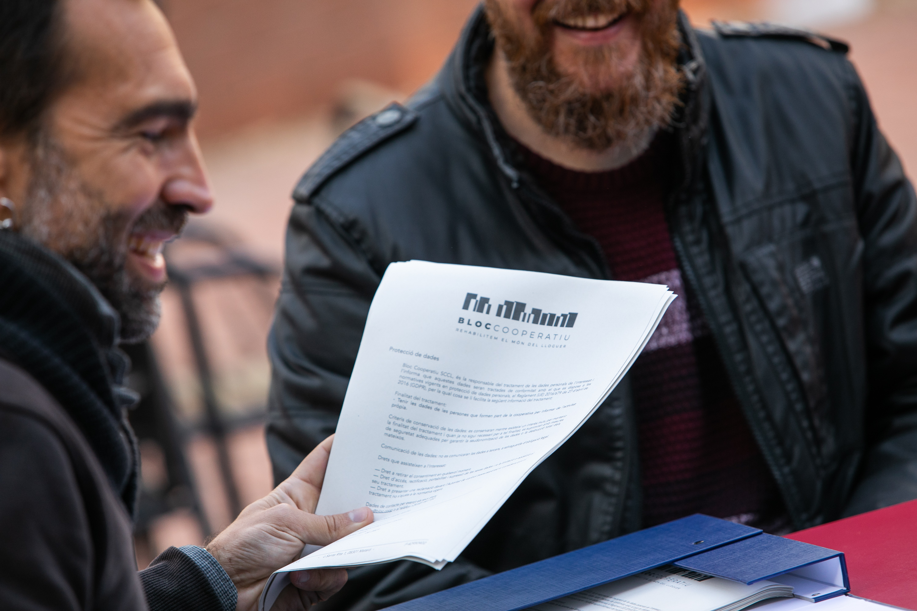 Two laughing men looking at a document (2021), (c)Bloc Cooperatiu